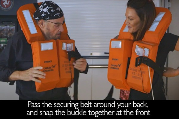 John Rhys-Davies and Karli Seed demonstrate how to put on a life jacket in the new safety video